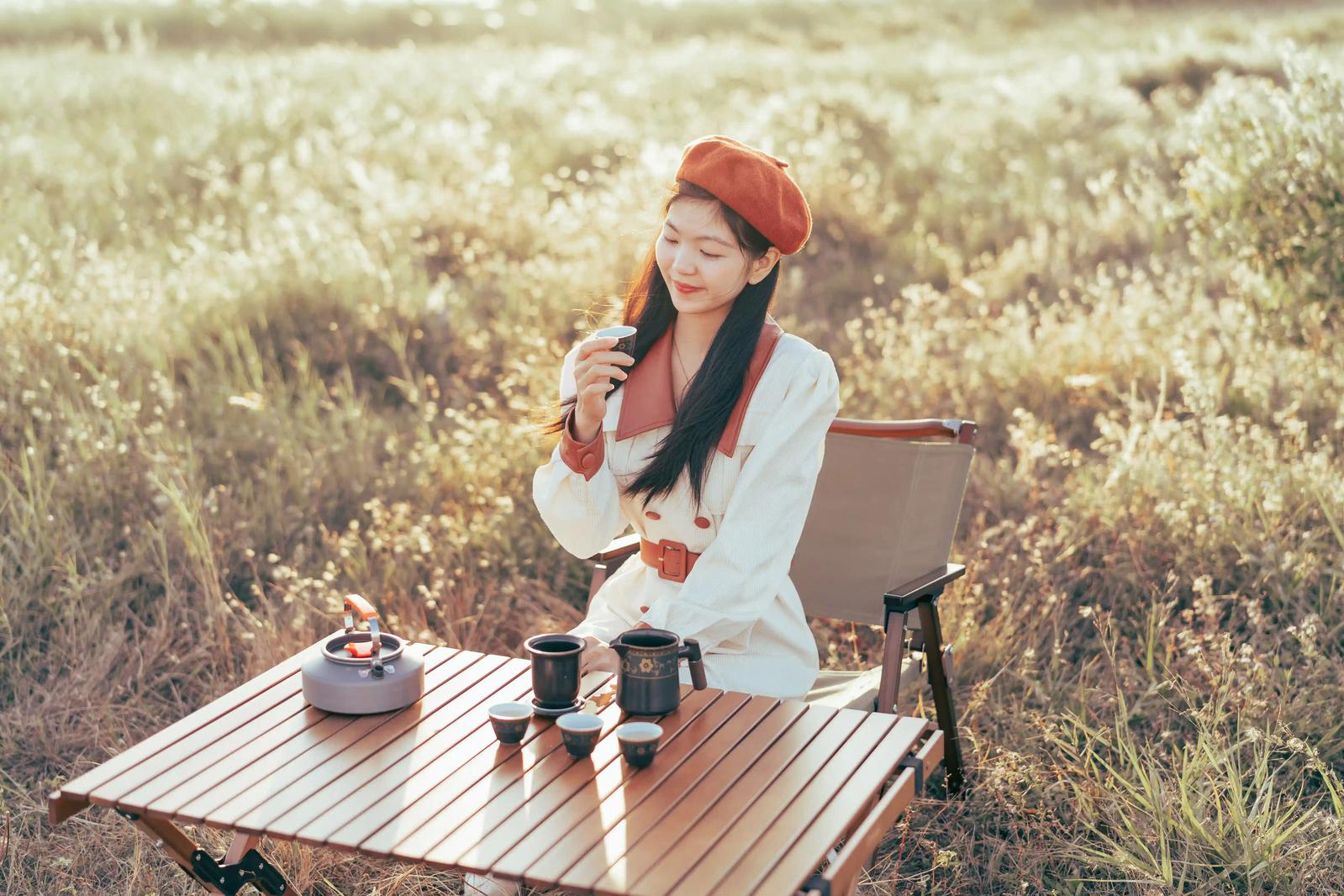 A young Chinese woman sitting in a field in the early morning, enjoying a cup of tea.