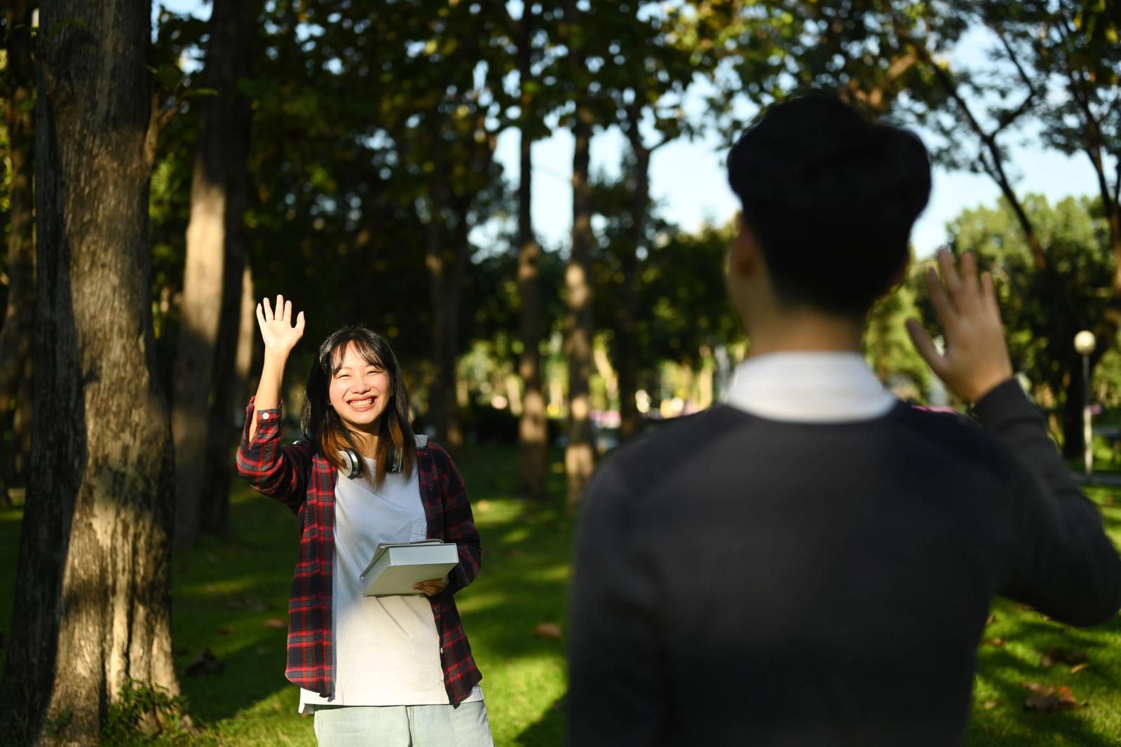 A young Chinese man and woman waving at each other, perhaps greeting each other after class.