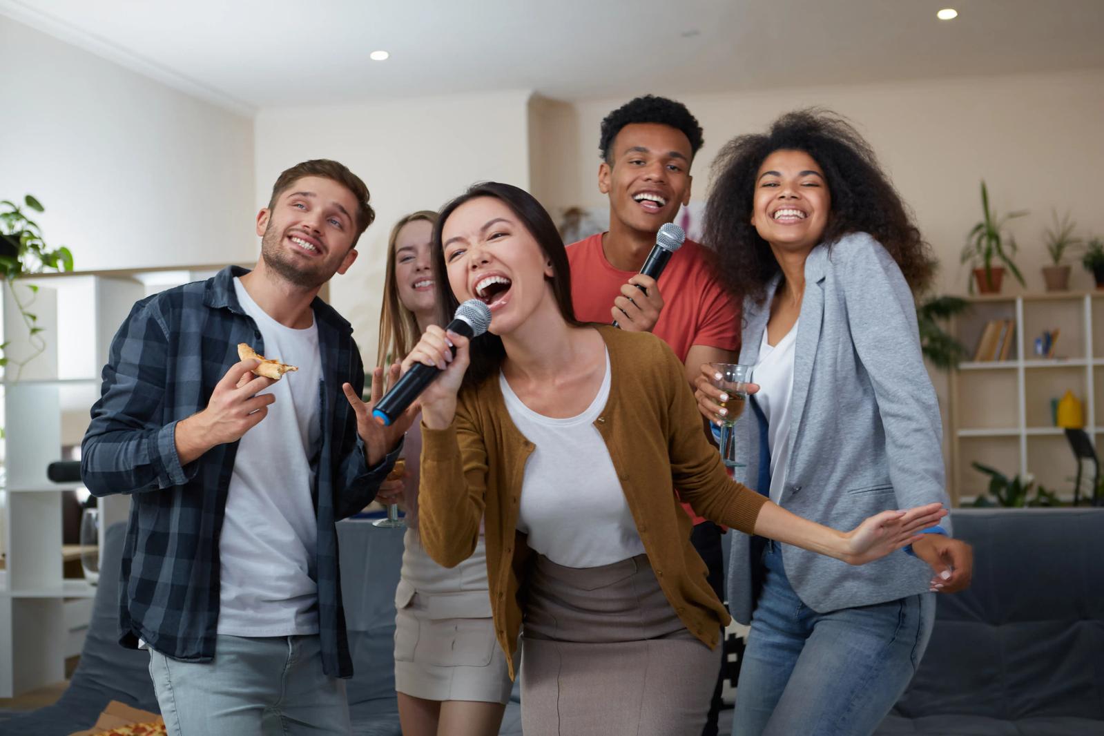 An Asian woman excitedly singing into a microphone, surrounded by her friends.