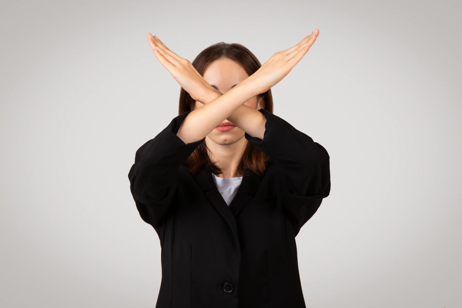 A Japanese woman with her arms crossed in front of her, forming a an X, a gesture that means "no".