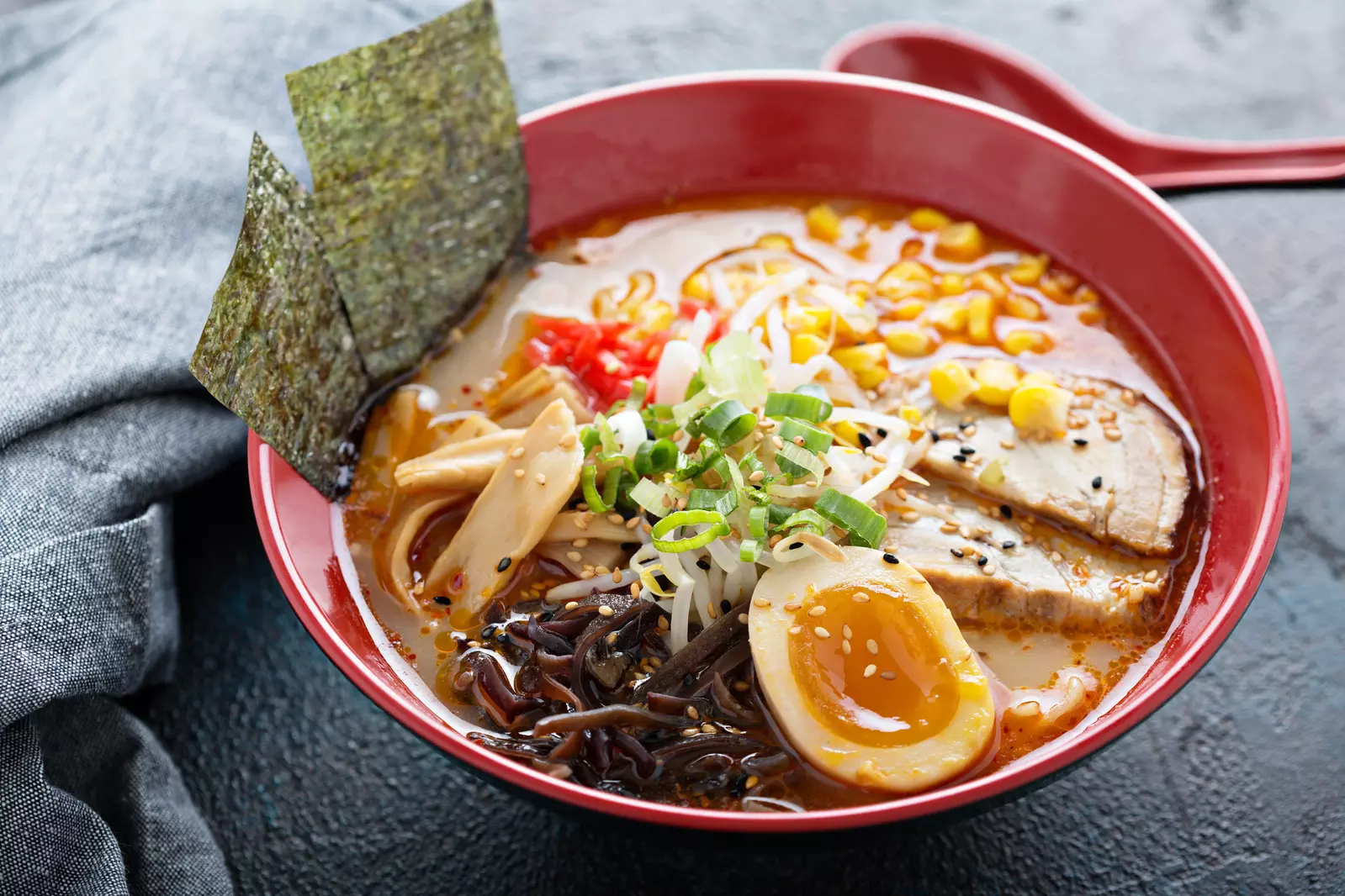 A bowl of Japanese ramen, a popular food, with pork, corn, and seaweed.