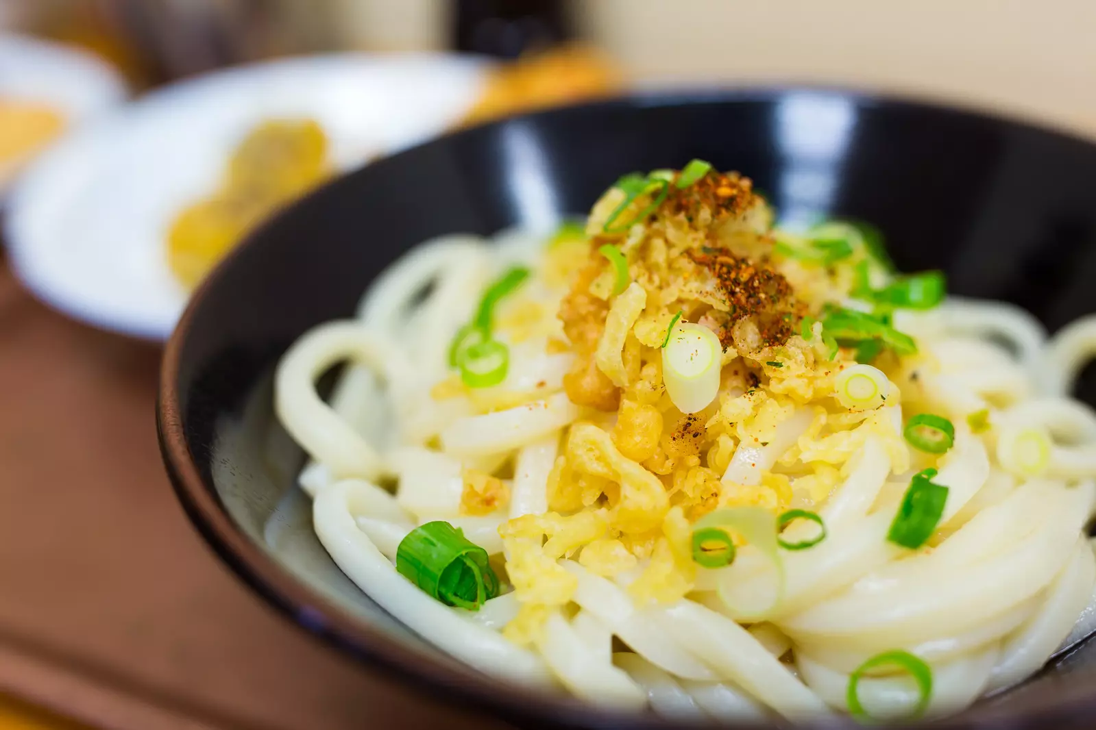 A bowl of Japanese udon noodles topped with green onions and crispy tempura flakes.