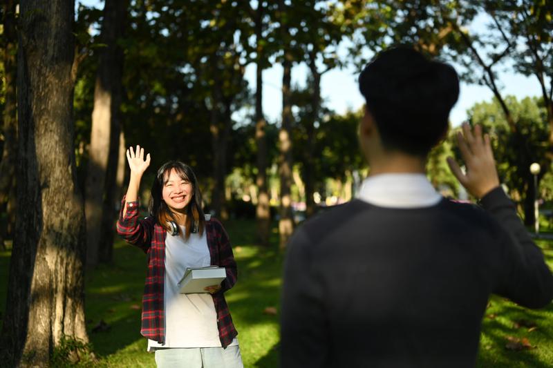 A young Chinese man and woman waving at each other, perhaps greeting each other after class.