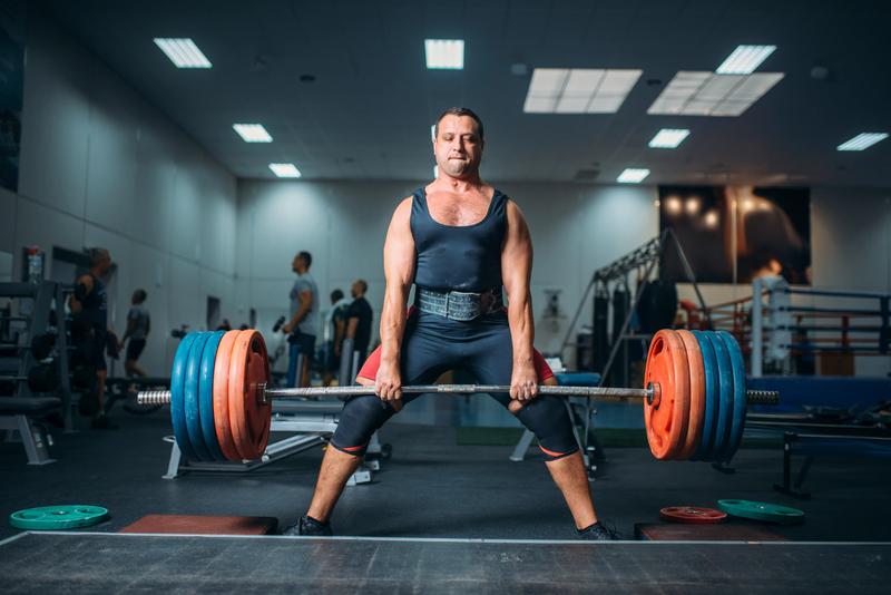 A photo of a man struggling to lift a heavy-looking barbell.