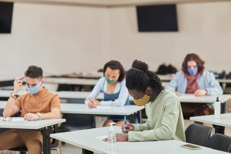 A group of several students sitting at tables and taking a test.