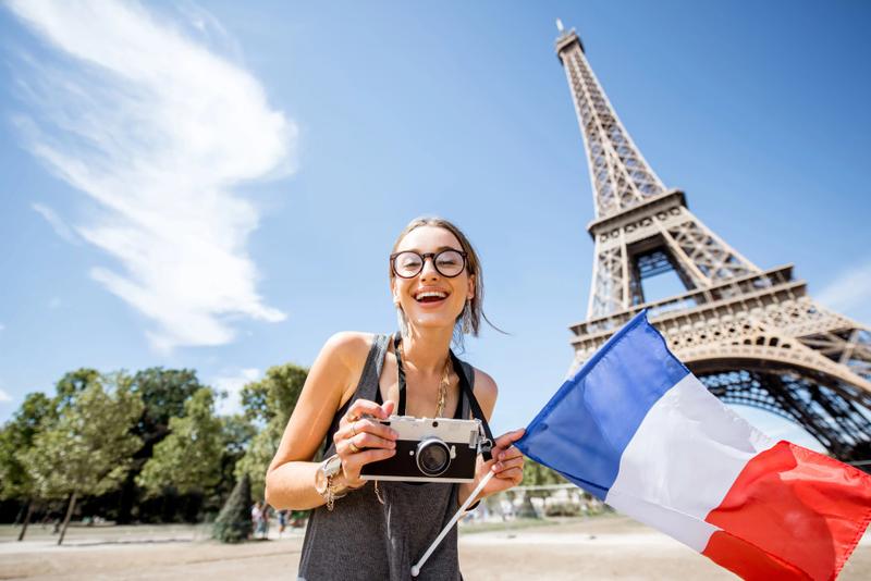 A woman holding a French flag standing in front of the Eiffel Tower.