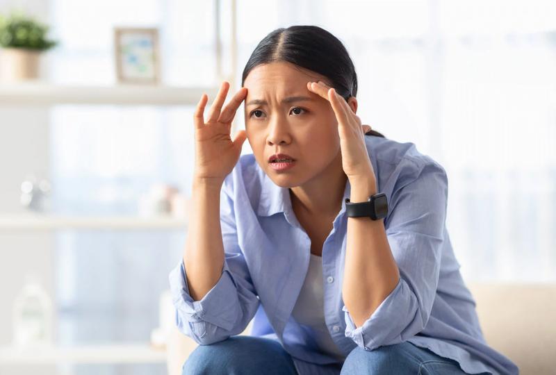 An Asian woman holding her head, wondering why English has to be so difficult and irregular.