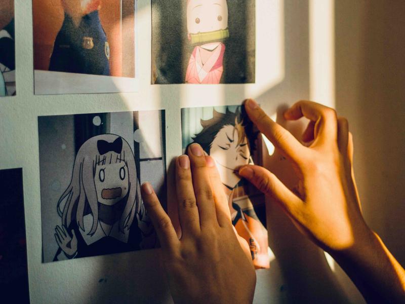 A photo of someone pinning pictures of manga characters onto their bedroom wall.