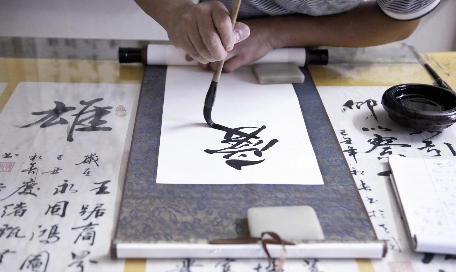 A Japanese person performing calligraphy with traditional tools.