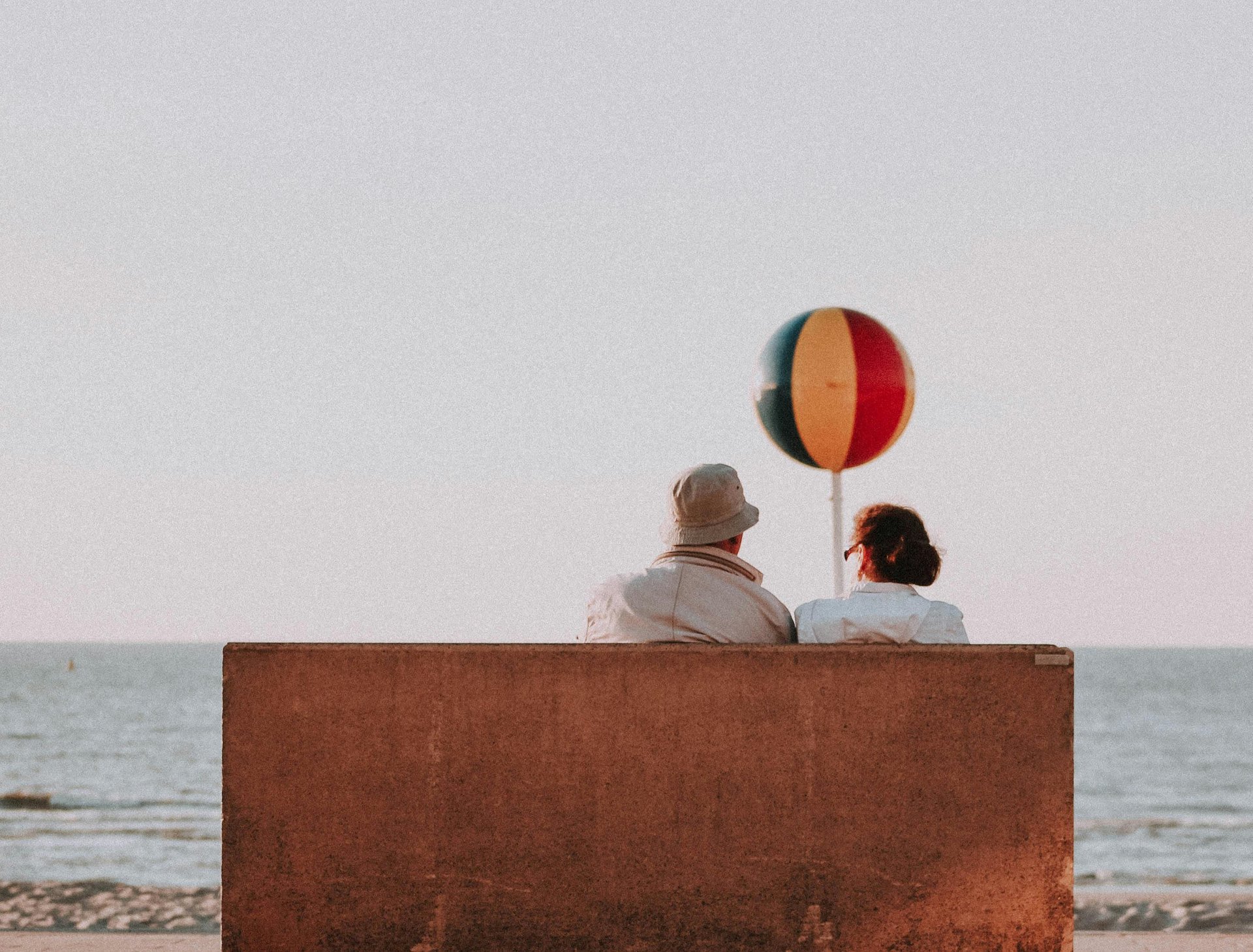 A couple sitting on a bench on a beach, reminiscing about someone they miss dearly